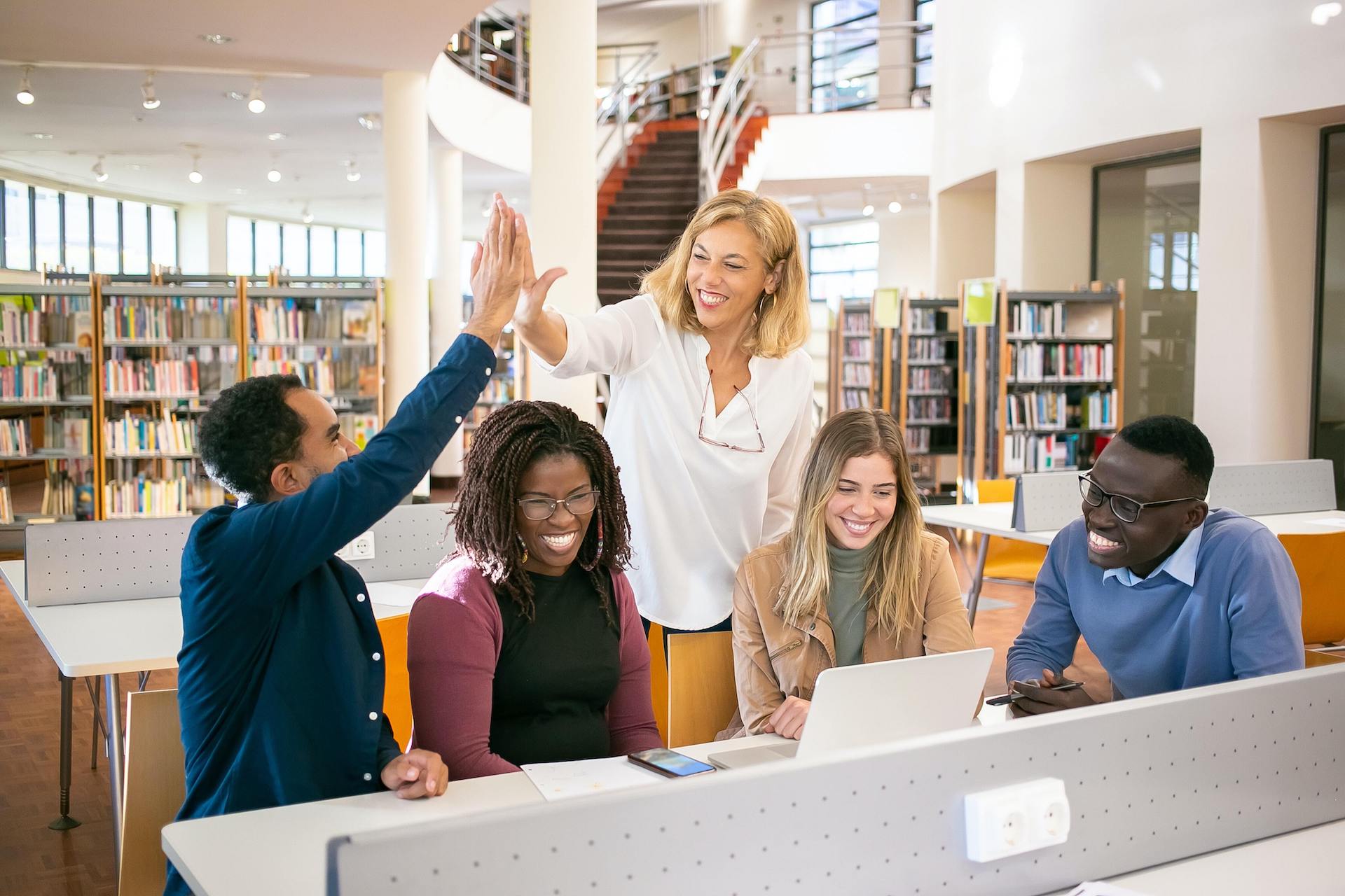 Group of people smile in library, man and woman high five