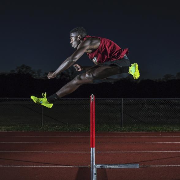 Division I athlete jumps hurdle on track