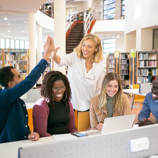 Group of people smile in library, man and woman high five