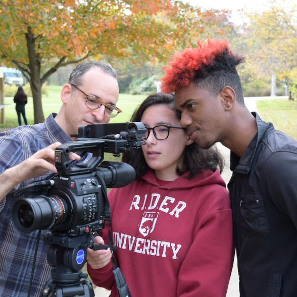 Two students and a professor looking through a large camera lens 