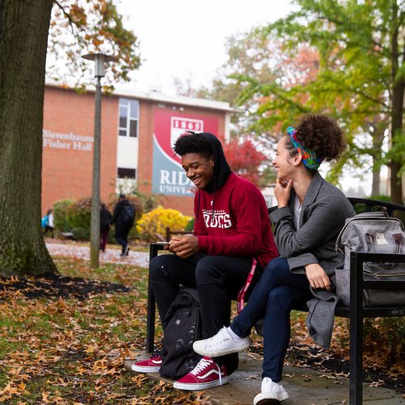 Students sit on bench talking on Rider campus.