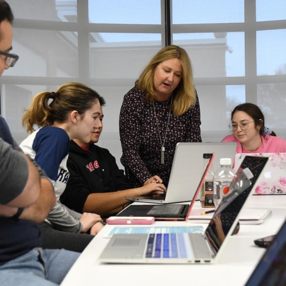 Female faculty member leans over group of students on laptop