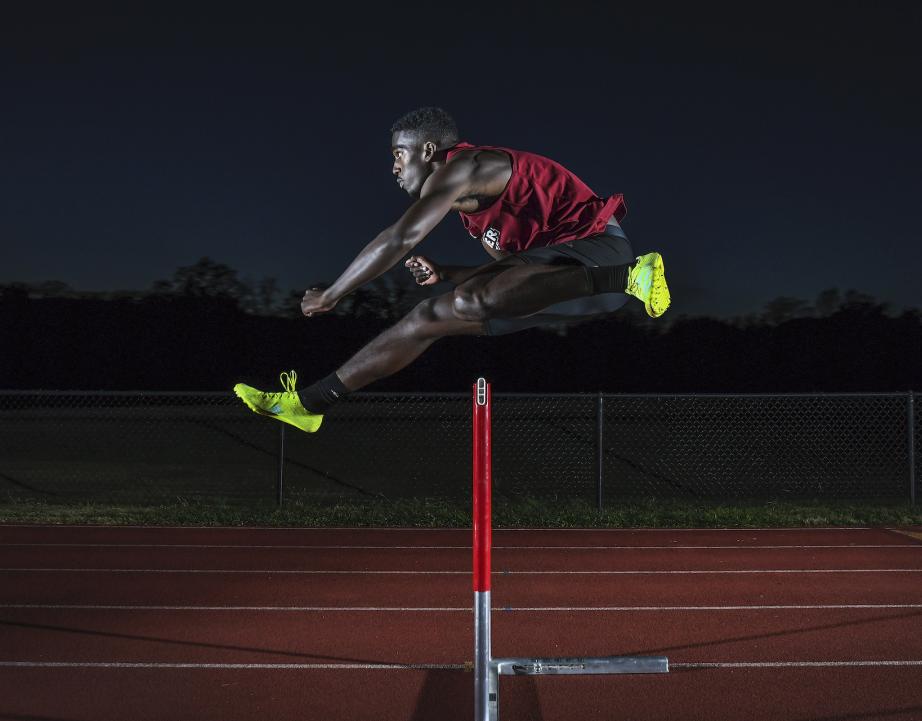 Division I athlete jumps hurdle on track